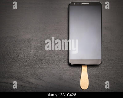 Handy auf einem Stick wie ein köstliches Dessert in Form von Schokolade popsicle auf einem dunklen Hintergrund Stockfoto
