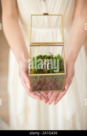 Mädchen in einem weißen Kleid hält ein Glas, in dem es gibt Hochzeit Ringe. Stockfoto