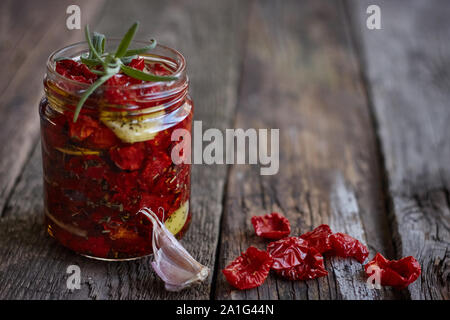Schließen Sie das Glas hausgemachten getrocknete Tomaten mit Kräutern der Provence, Knoblauch und Olivenöl auf eine rustikale Holz- Oberfläche, selektiver Fokus Stockfoto