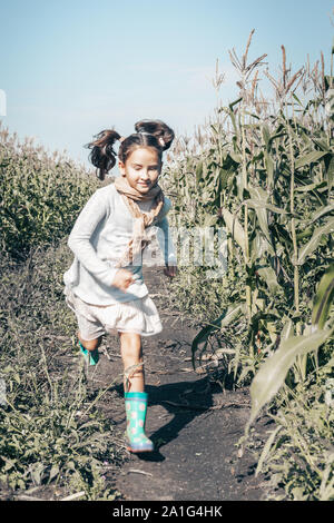 Gerne kleine Mädchen läuft durch Kornfeld. Froh, dass weibliches Kind in legere Kleidung outdoor. Lächelnd Kind im Dorf. Mädchen mit zufriedenen Gesicht expressio Stockfoto