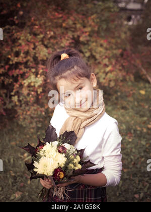 Schwere kleine Mädchen mit Blumen und Blätter Bouquet. Kind in der Schule uniform Outdoor. Schulmädchen portrait. Mädchen mit nachdenklichen Gesichtsausdruck. Stockfoto