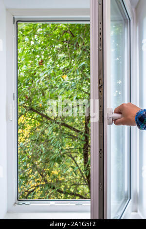 Mann öffnet sich PVC-Fenster, das Sie grün von einem Baum Park in der ökologisch sauberen Gegend der Stadt sehen können mit frischer Luft Stockfoto