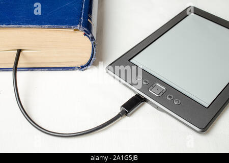 EBook auf den alten dicken blauen Buch mit einem Kabel angeschlossen, und laden Sie die Informationen von dort auf einem hellen Hintergrund Stockfoto