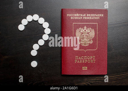 Reisepass der Bürger der Russischen Föderation ist auf einem hölzernen Tisch, in der Nähe von medizinischen Pillen in Form eines Fragezeichens gestapelt Stockfoto