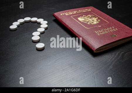Reisepass der Bürger der Russischen Föderation ist auf einem hölzernen Tisch, in der Nähe von medizinischen Pillen in Form eines Fragezeichens gestapelt Stockfoto