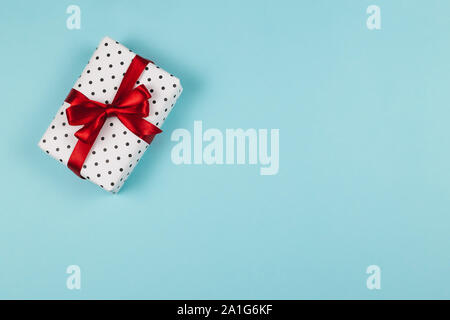 Geschenkbox verpackt in schwarz Polka-dot Weißbuch mit roter Schleife auf blauem Hintergrund. Urlaub Konzept. Stockfoto