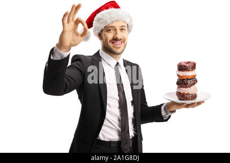 Geschäftsmann mit einer Platte von Donuts tragen ein Weihnachtsmann Mütze und Gestik, die sich perfekt mit den Fingern auf weißem Hintergrund Stockfoto