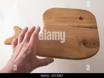 Eine männliche Hand erreichen für einen handgefertigten Holzmöbeln Charcuterie Bord von butternut Holz, in der Form eines Wals. Stockfoto