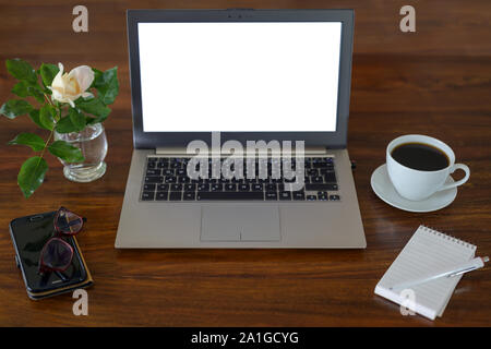 Mock up, Laptop mit leeren weißen Bildschirm auf einem Schreibtisch aus Holz mit Notepad, Gläser, Kaffeetasse, Telefon und eine Blume, business Arbeitsbereich in einem Büro, kopieren Stockfoto