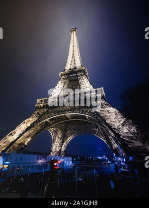 Paris, Frankreich - 20 Jan, 2019: Wide Low Angle View von ikonischen Paris Eiffel Tower mit Besuchern von Paris entdecken das Denkmal bei Nacht Blue Mist Farbe Stockfoto