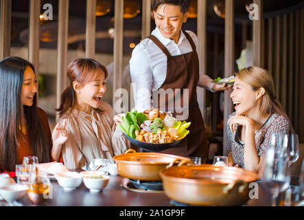 Kellner bringen Gemüse für Hot Pot und mit einer Gruppe von Freunden im Restaurant Stockfoto