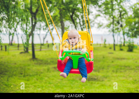 Happy little boy reiten auf einer Schaukel in einem Park. Stockfoto