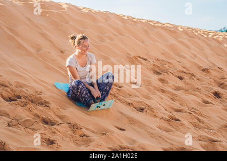 Junge Frau rollt auf eine Rodelbahn im Schlitten in der Wüste. Stockfoto