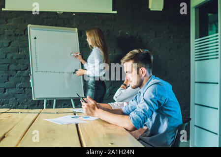 Langweilige Präsentation. Gruppe junger Geschäftsleute in Smart Casual Wear gelangweilt beim zusammen am Tisch sitzen und Wegsehen. Stockfoto