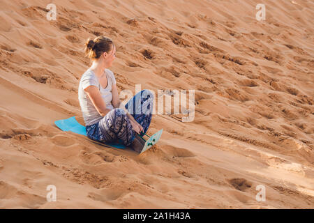 Junge Frau rollt auf eine Rodelbahn im Schlitten in der Wüste. Stockfoto