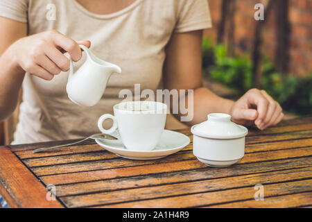 Woman's Hand gießen Milch in weißen Tasse Kaffee im Café im Freien. Stockfoto