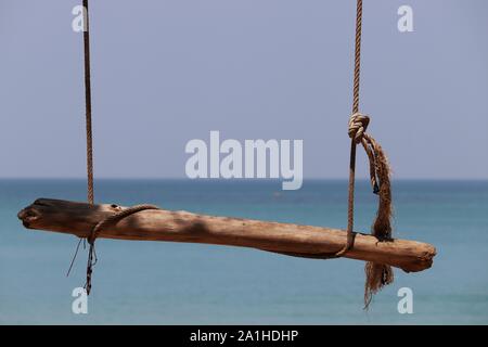 Swing von Log- und Seile auf einem Hintergrund von blauem Meer und Himmel. Strand Ferienhäuser, Konzept von Freiheit, Glück und Romantik Stockfoto