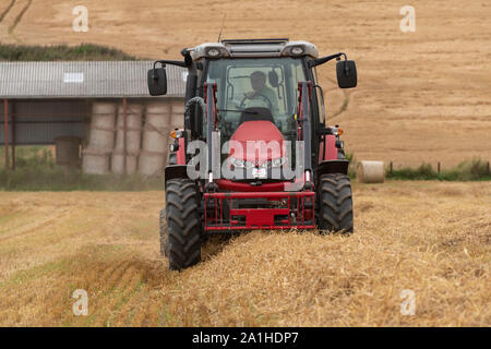 Um eine vordere oder gegen die Wand, mit Blick auf ein Landwirt Pressen von Stroh in einem Feld von Stoppeln. Stockfoto