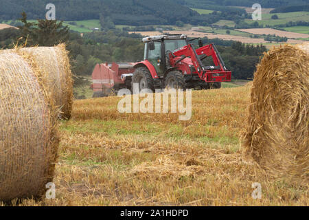 Ein Landwirt Pressen von Stroh auf einem Hügel mit Blick auf den Wald, Wald und Ackerland Stockfoto