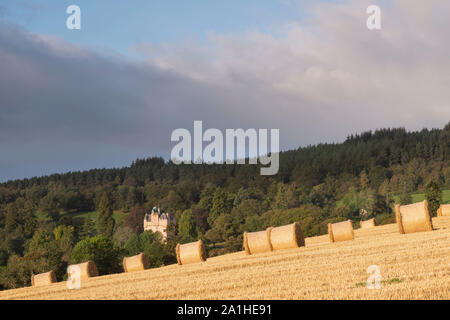 Ein Blick auf Strohballen sitzend in einen Drei-tage-Feld, mit Craigievar Castle auf einem bewaldeten Hügel im Hintergrund Stockfoto