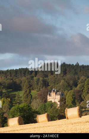 Ein Blick auf Strohballen sitzend in einen Drei-tage-Feld, mit Craigievar Castle auf einem bewaldeten Hügel im Hintergrund Stockfoto