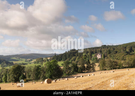 Ein Blick über die hügelige Landschaft in Aberdeenshire, mit einem Feld von Strohballen und Craigievar Castle eingebettet auf einem bewaldeten Hügel mit Blick auf Ackerland Stockfoto