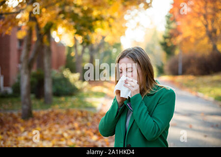 Kranke junge Frau mit Kälte und Grippe stehen im Freien, Niesen, wischen Nase mit Taschentuch, Husten. Herbst Straße Hintergrund Stockfoto