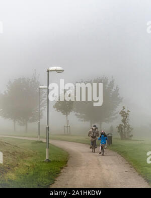 Ein Vater und eine Tochter Zyklus auf Ackerland Pfad in einer kalten, nebligen Morgen Stockfoto