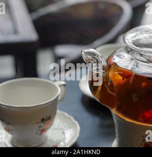 Schwarzer Tee mit goji (chinese wolfberries) und Jasmin Teekanne aus Glas und Porzellan Tasse mit Untertasse Blumenmuster auf schwarz Tabelle Stockfoto