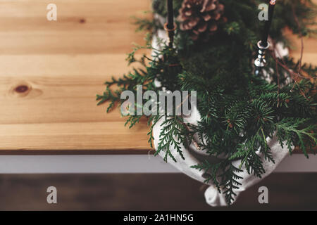 Stilvolle rustikale Weihnachten arrangement für festliche Abendessen Nahaufnahme. Tannenzweigen mit Tannenzapfen und vintage Leuchter mit schwarzen Kerzen auf Leinen clot Stockfoto