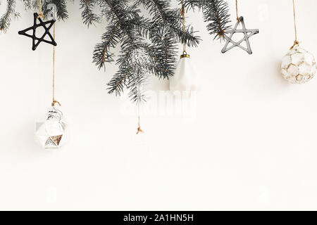 Stilvolle Weihnachten Ornamente auf Tanne Zweig hängend auf der weißen Wand. Kreative Weihnachten festliche Dekoration. Kiefer Zweig mit Vintage Glas Spielzeug. Moderne Zusätzl Stockfoto