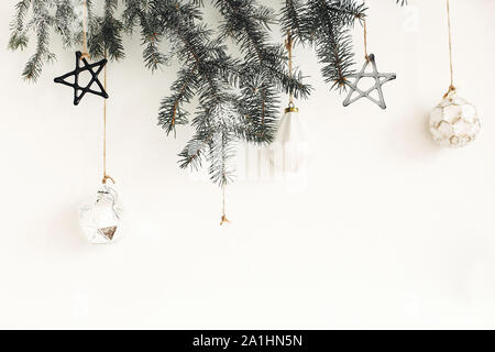 Stilvolle Weihnachten Ornamente auf Tanne Zweig hängend auf der weißen Wand. Kreative Weihnachten festliche Dekoration. Kiefer Zweig mit Vintage Glas Spielzeug. Moderne Zusätzl Stockfoto