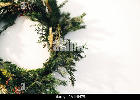 Rustikale weihnachten Kranz aus Kiefernzweigen, Kegel und Beeren auf weiße Wand Nahaufnahme. Stilvolle weihnachten Kranz. Skandinavische minimalistischen Dekor. Jahreszeit" Stockfoto