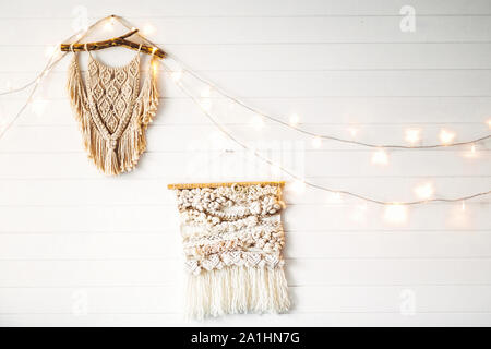 Macrame an den weißen Holzwand mit Beleuchtung. Stilvolle boho Einrichtung, moderne Wand hängen. Moderne Einrichtung im skandinavischen oder Zimmer im Landhausstil. Stockfoto