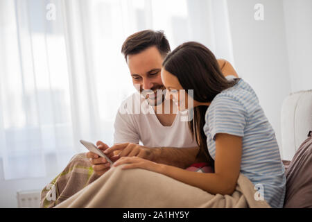 Junge glückliches Paar auf Smartphone im Bett in den Morgen. Stockfoto