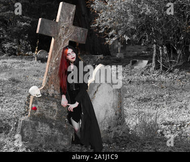 Dunkle und geheimnisvolle junge Frau in Schwarz gothic Kostüm spricht mit menschlichen Schädel in der mittelalterlichen Kirche Friedhof gekleidet Stockfoto