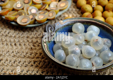 Sicht von oben Vietnamesischen tropischen Süß, wässrige Fruchtfleisch Frucht, die in der Nähe Longanfrüchte Fleisch in transluzent Weiß auf Schwarz Platte mit einem schwarzen Samen, gelbe Schale, Stockfoto