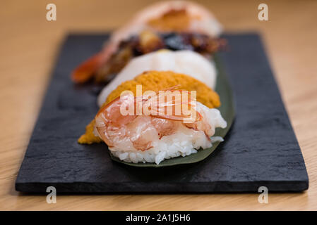 Detail der gedämpfte Garnelen nigiri, mit Hintergrund der Nigiri mit Pacific Seeigel, gedünsteter Lachs, gedämpfte Garnelen, Kaviar, gebratener Aal und Squid, Holz Stockfoto