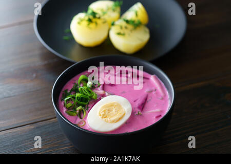 Litauische Saltibarsciai (Kalt Rüben Suppe) mit hart gekochten Eiern und Kartoffeln, gewürzt mit Frühlingszwiebeln und Dill. Dunkler Holztisch, hohe Auflösung Stockfoto