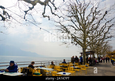Vevey, Schweiz - April 2019: Touristen am Ufer des Genfer See von Vevey, Kanton Waadt, Schweiz. Alpen im Hintergrund. Stockfoto