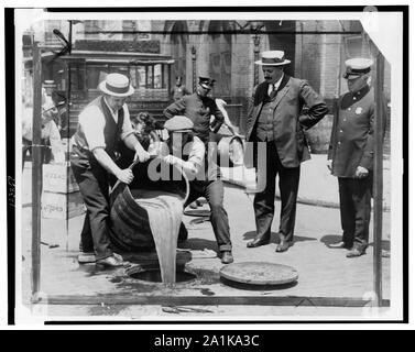 New York City Stellvertretender Polizeichef John A. Leach, rechts, beobachten Agenten gießen Schnaps in die Kanalisation nach einer Razzia auf dem Höhepunkt der Prohibition Stockfoto