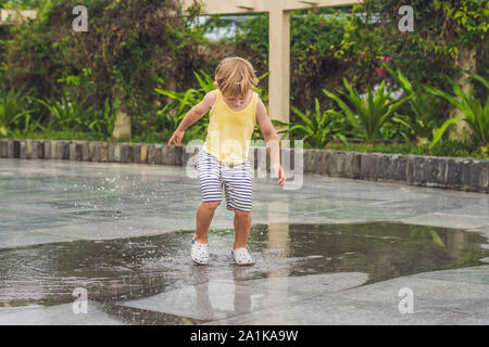 Kleiner Junge läuft durch eine Pfütze. Sommer im Freien Stockfoto