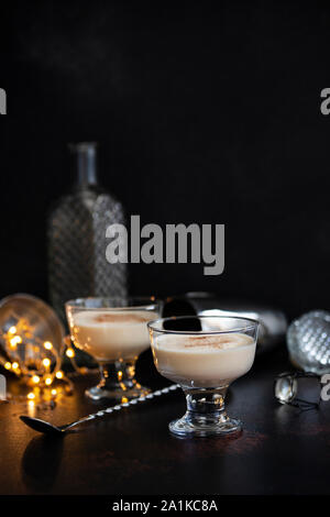 Eierlikör traditionelle Weihnachten alkoholisches Getränk mit Zimt und Muskatnuss in zwei Gläser auf einen dunklen Tisch mit Bar Tools und Weihnachtsschmuck. Winter Stockfoto