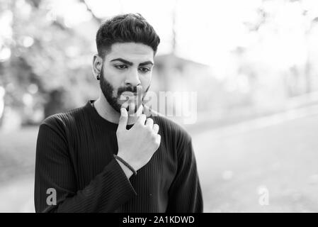 Junge schöne Indische Mann Denken mit der Hand am Kinn im Park Stockfoto