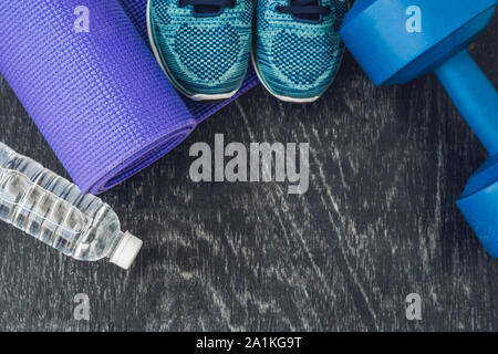 Yoga Matte, Sportschuhe, Hanteln und eine Flasche Wasser auf blauem Hintergrund. Konzept gesunder Lebensstil, Sport und Ernährung. Sport Equipment. Platz kopieren Stockfoto