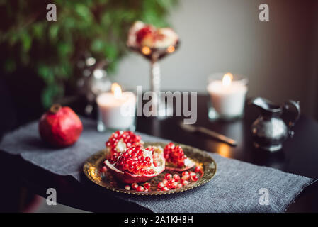 Noch immer leben Zusammensetzung mit saftigen Red cut gelöscht Granatapfel auf einer Kupferplatte, brennende Kerzen und andere orientalische Einrichtung auf dem Schwarzen Tisch. Weich sel Stockfoto
