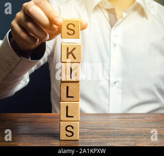 Ein Mann legt Holzblöcke mit dem Wort Fähigkeiten. Wissen und Fähigkeiten. Selbstverbesserung. Bildung Konzept. Ausbildung. Führungsqualitäten. Menschliche Fähigkeiten Stockfoto