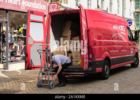 Postman eine Lieferung von einem Paket Kraft van voller Kisten in einer Einkaufsstraße. Stamford, Lincolnshire, England, Vereinigtes Königreich, Großbritannien Stockfoto