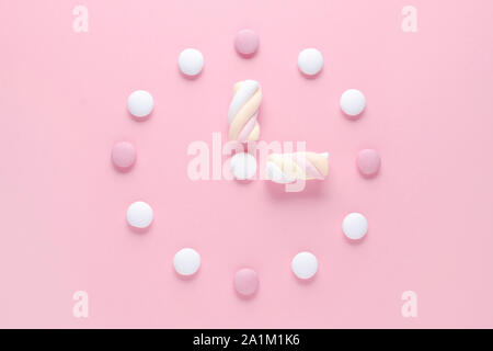 Konzept Bild, eine Uhr mit Süßigkeiten und Marshmallow, Pastellfarben auf Rosa Stockfoto