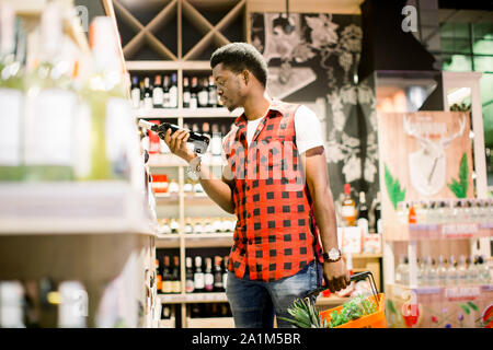 Afrikanischer mann Einkaufen in Wein im Supermarkt. Schwarzer Mann einkaufen, die am Markt beim kaufen Wein. Hübscher Kerl holding Warenkorb Stockfoto